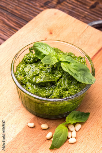 Fresh pesto in small glass bowl on wooden background