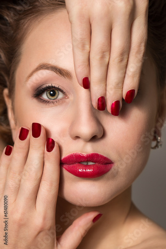 Model with red lips covering face with hands with red nails.