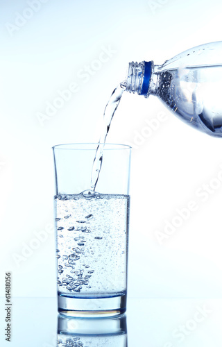 Pour water from bottle into glass, on light blue background