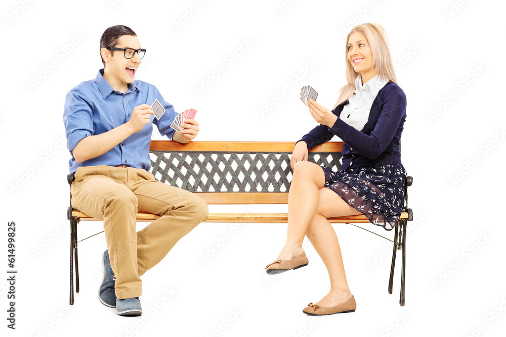 Fototapeta premium Young couple playing cards seated on wooden bench