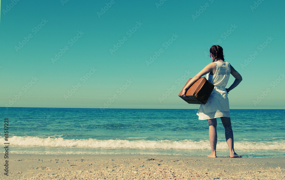 woman with suitcase on the beach. Photo in old image style.