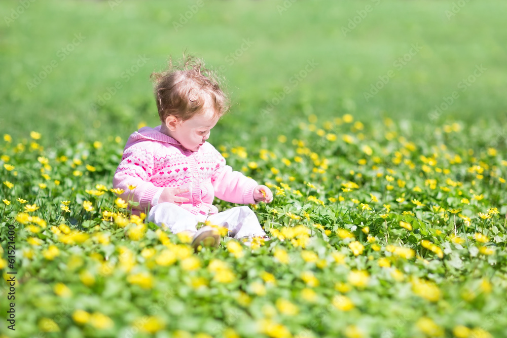 Adorable baby girl playing with yellow flowers in a park
