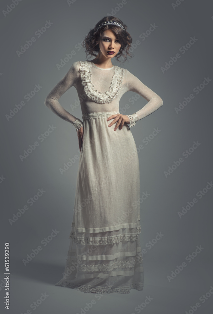 Elegant young woman in white long dress posing indoors Elegant young woman in white long dress posing indoors