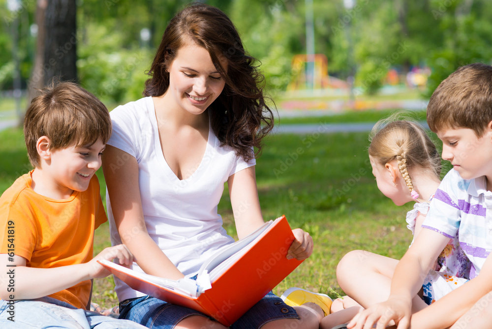 teacher reads a book to children in a summer park teacher reads a book to children in a summer park