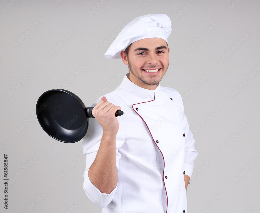 Professional chef in white uniform and hat, holding pan in his Professional chef in white uniform and hat, holding pan in his