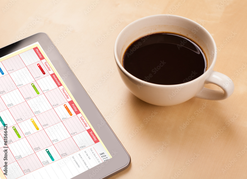 Tablet pc showing calendar on screen with a cup of coffee on a d Tablet pc showing calendar on screen with a cup of coffee on a d