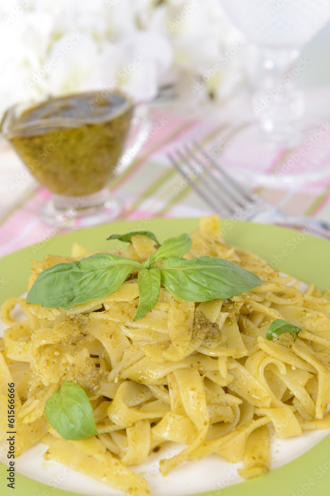 Delicious pasta with pesto on plate on table on light Delicious pasta with pesto on plate on table on light