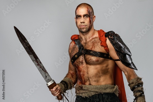 Wounded gladiator with sword covered in blood isolated on grey