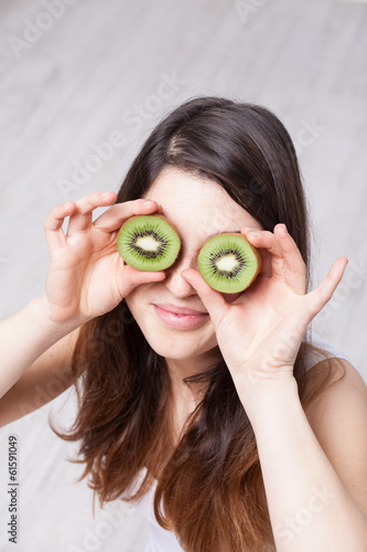 Young Woman Holding Kiwi Slices in Front of Eyes