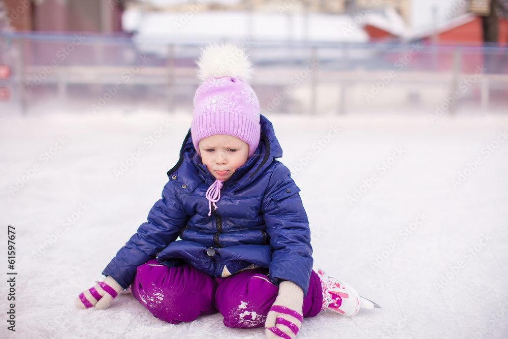 Little sad girl sitting on ice with skates after the fall Little sad girl sitting on ice with skates after the fall