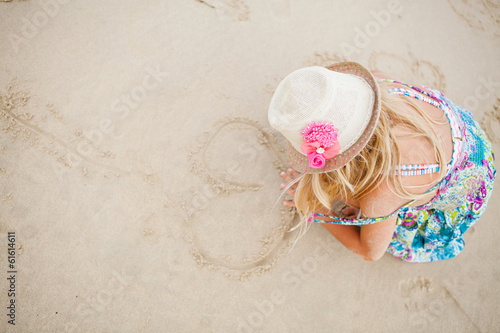 Young girl drawing heart shapes in sand