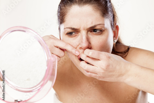 young woman squeeze her acne in front of the mirror photo