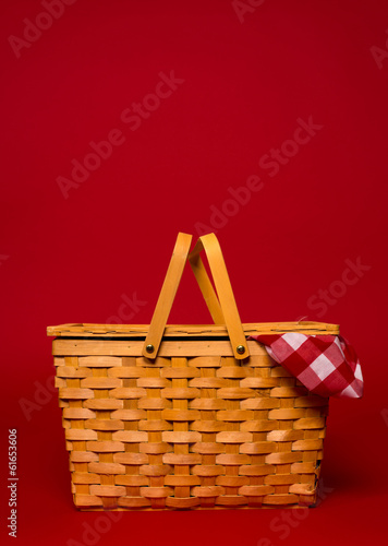 A wicker picnic basket with red gingham tablecloth on a red back