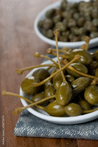 two kinds of pickled capers on wooden table