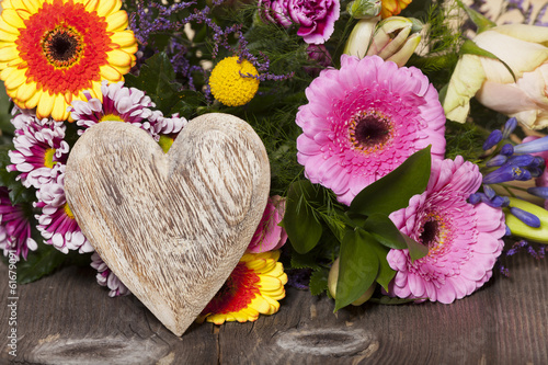 Rustikales Holzherz vor einem Blumenstrauß auf Holztisch