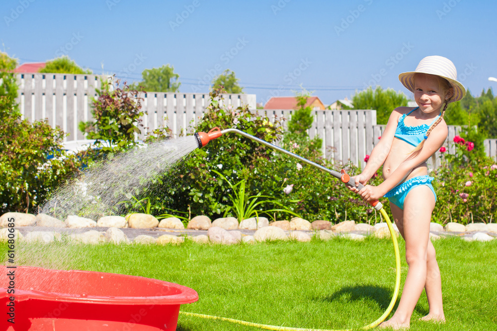 Adorable little girl pouring water from hose and laughing
