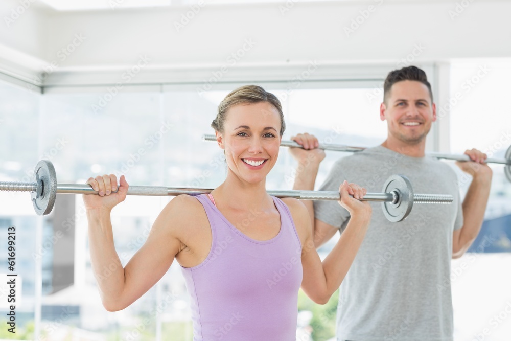 Woman and man lifting barbells at fitness studio
