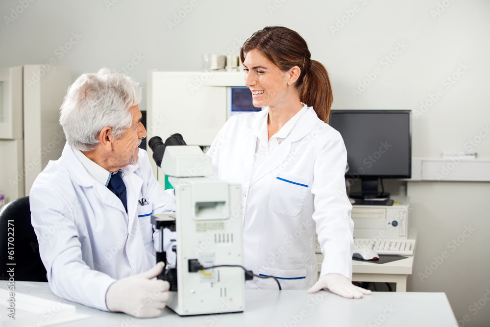 Scientist Discussing With Colleague While Using Microscope Scientist Discussing With Colleague While Using Microscope