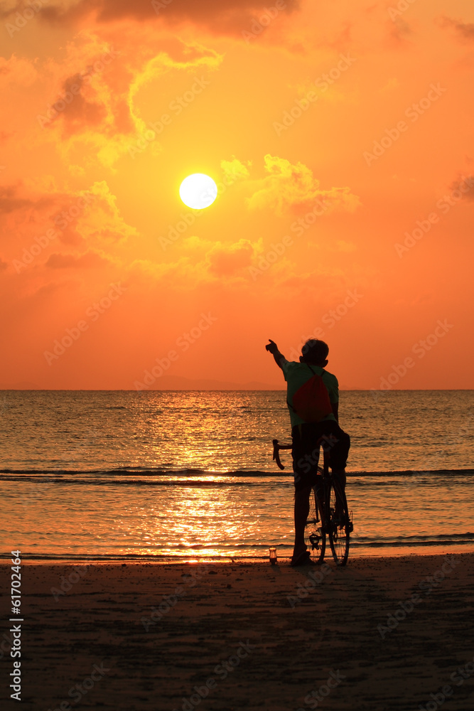 Fototapeta premium Silhouette of a biker on the beach point to sunset