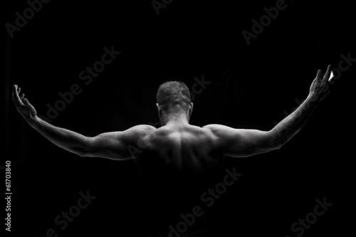Rear view of a muscular man with arms stretched out on black bac