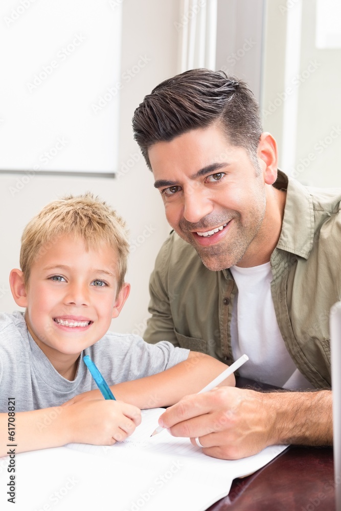 Happy father and son sitting at table colouring together Happy father and son sitting at table colouring together