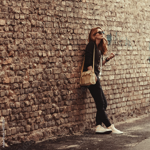 Beautiful fashionable girl stands near the brick wall