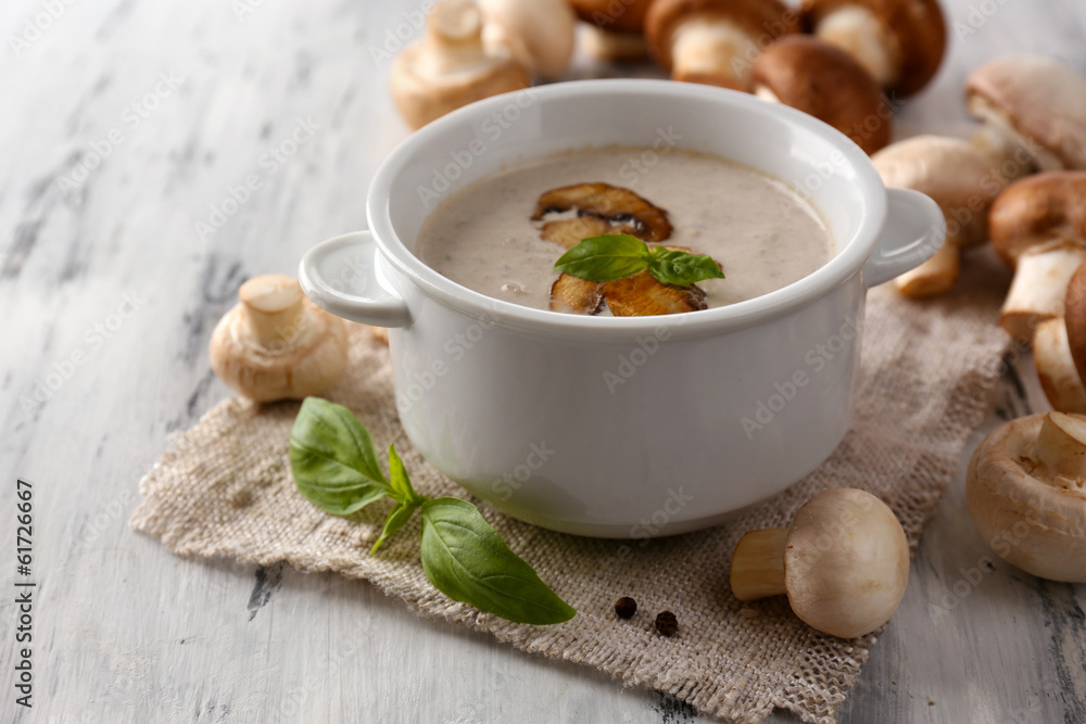 Mushroom soup in white pot, on napkin, on wooden background Mushroom soup in white pot, on napkin, on wooden background