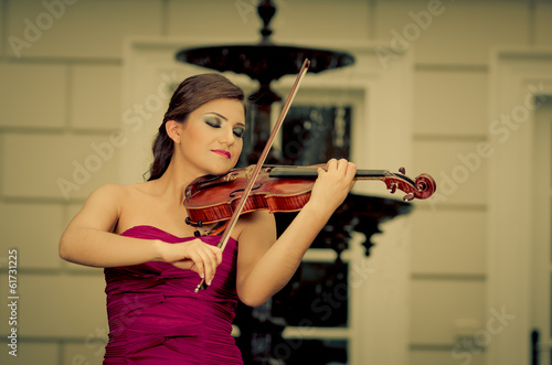 Beautiful brunette woman with a violin in her hands. fountain