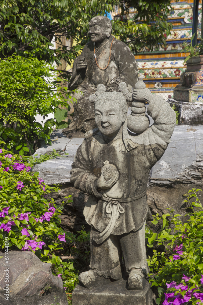 Statue of little Chinese girl with a monk in green garden in Ban