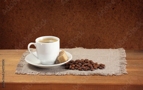 Coffee beans, cup, saucer, sugar, napkin on wooden table
