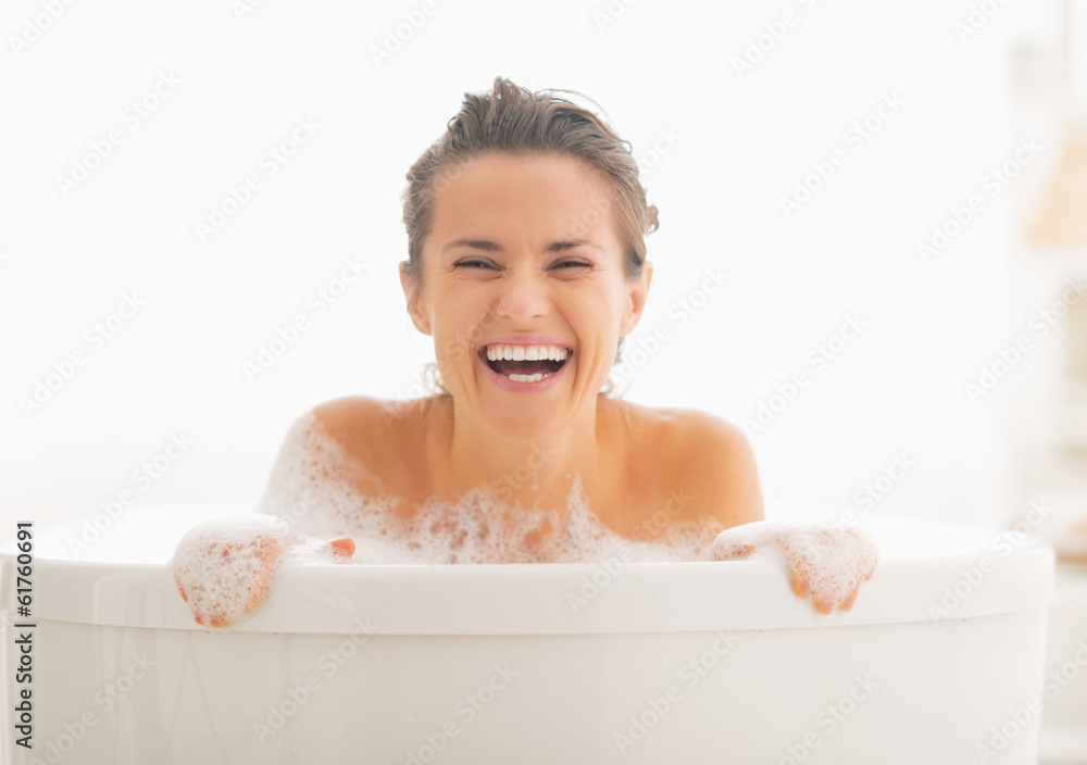 Smiling young woman looking out from bathtub Smiling young woman looking out from bathtub