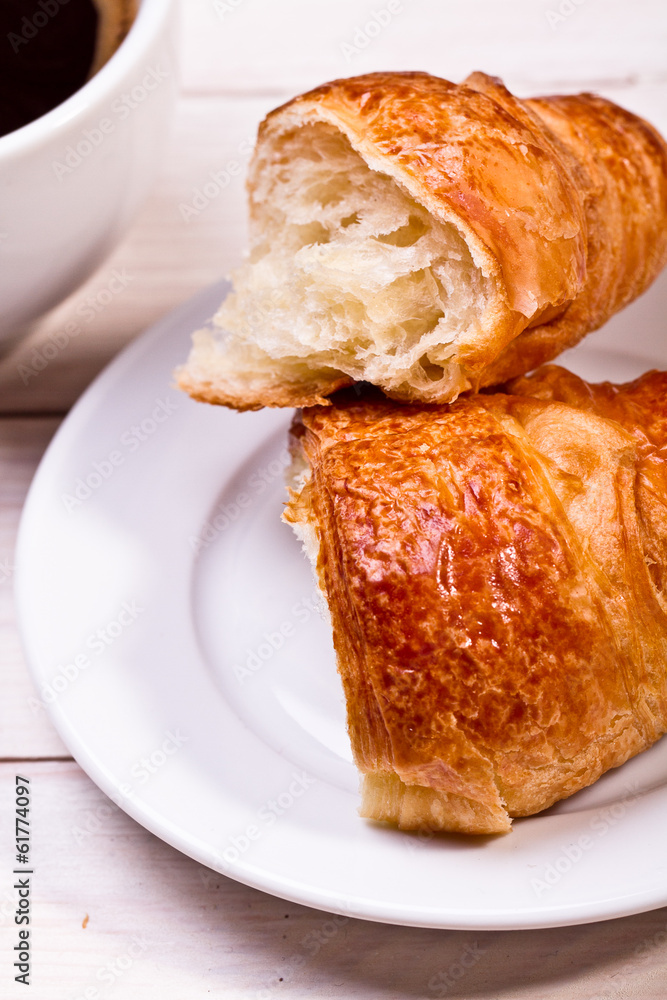 Coffee cup with a croissant isolated on wooden table Coffee cup with a croissant isolated on wooden table