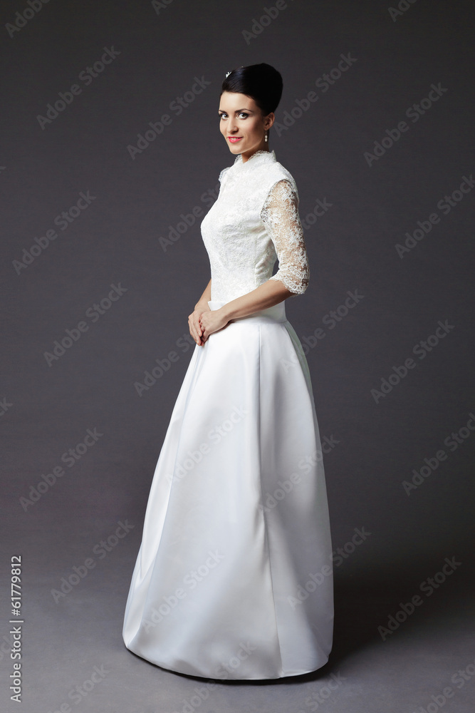 The beautiful young woman posing in a wedding dress on a grey ba The beautiful young woman posing in a wedding dress on a grey ba