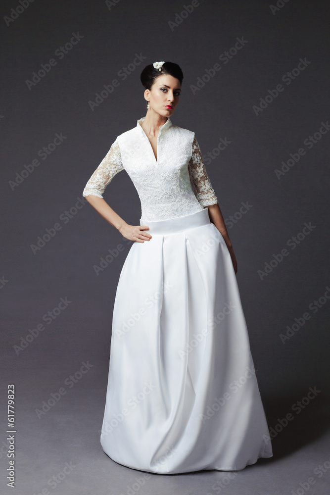 The beautiful young woman posing in a wedding dress on a grey ba