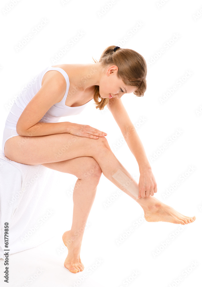 Young woman waxing her legs applying a strip, isolated Young woman waxing her legs applying a strip, isolated