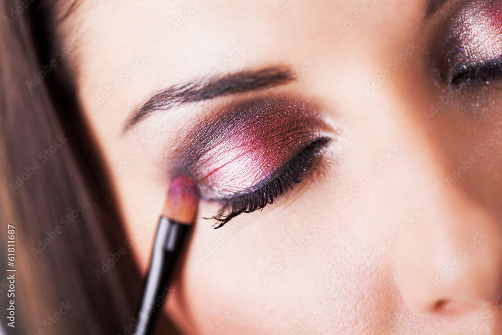 Attractive young woman applying eyeshadow.