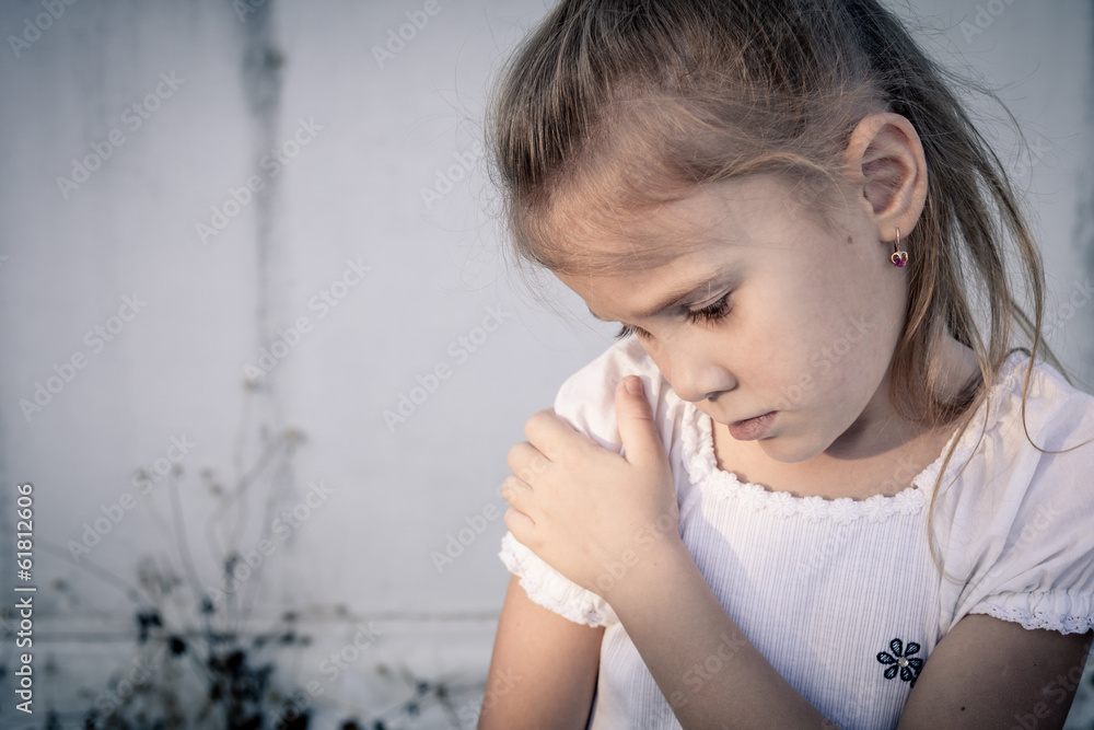 Portrait of sad little girl sitting near wall in the day time Portrait of sad little girl sitting near wall in the day time