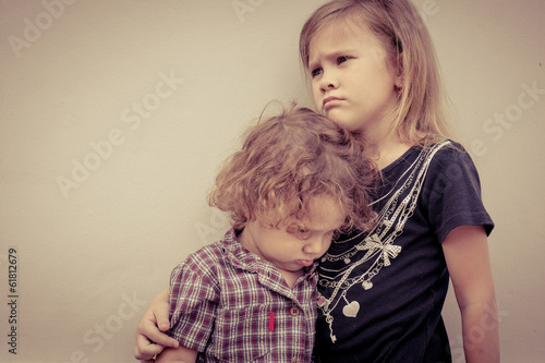 Portrait of sad little girl and little boy standing near wall in