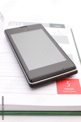 Modern mobile phone lying on open calendar