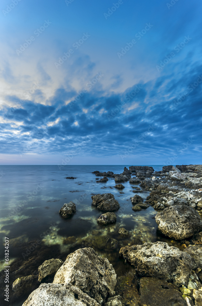 The rocky shore of the peaceful ocean at sunset