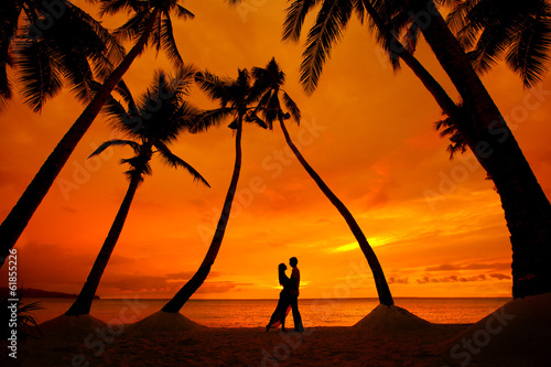 couple kissing at tropical beach with palm trees with sunset in photo
