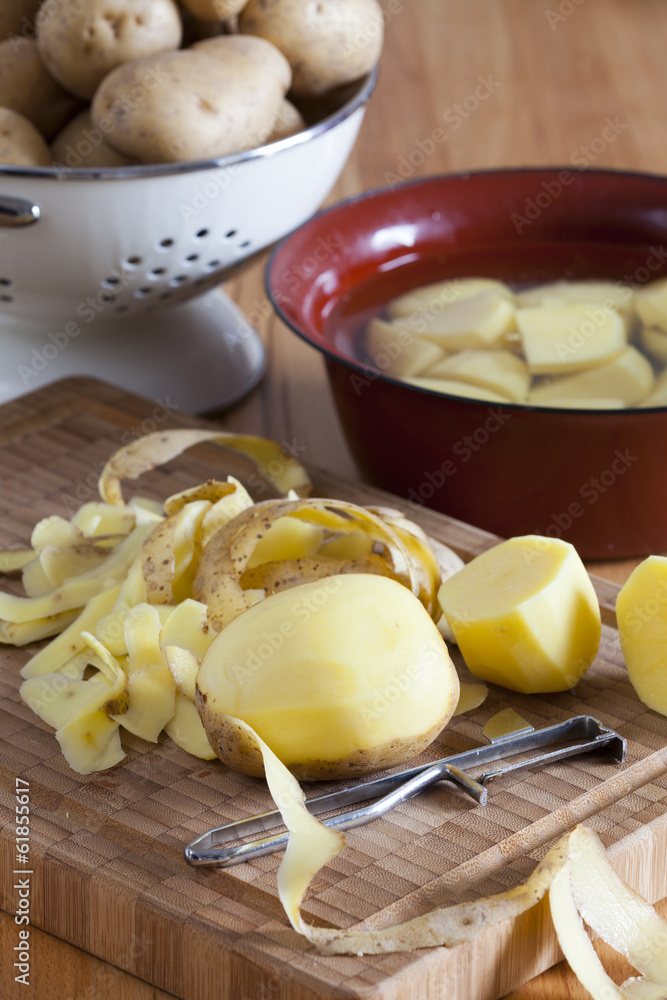 Kartoffeln und Kartoffelschäler auf Schneidebrett Kartoffeln und Kartoffelschäler auf Schneidebrett