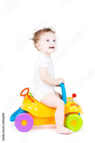 Cute baby with curly hair on a toy car