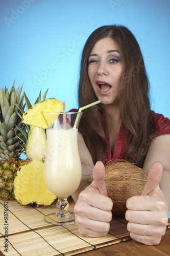 Junge Frau mit Pina-Colada, Ananas und Kokosnuss am Esstisch