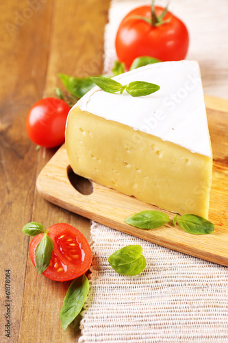 Tasty Camembert cheese with tomatoes and basil, on wooden table