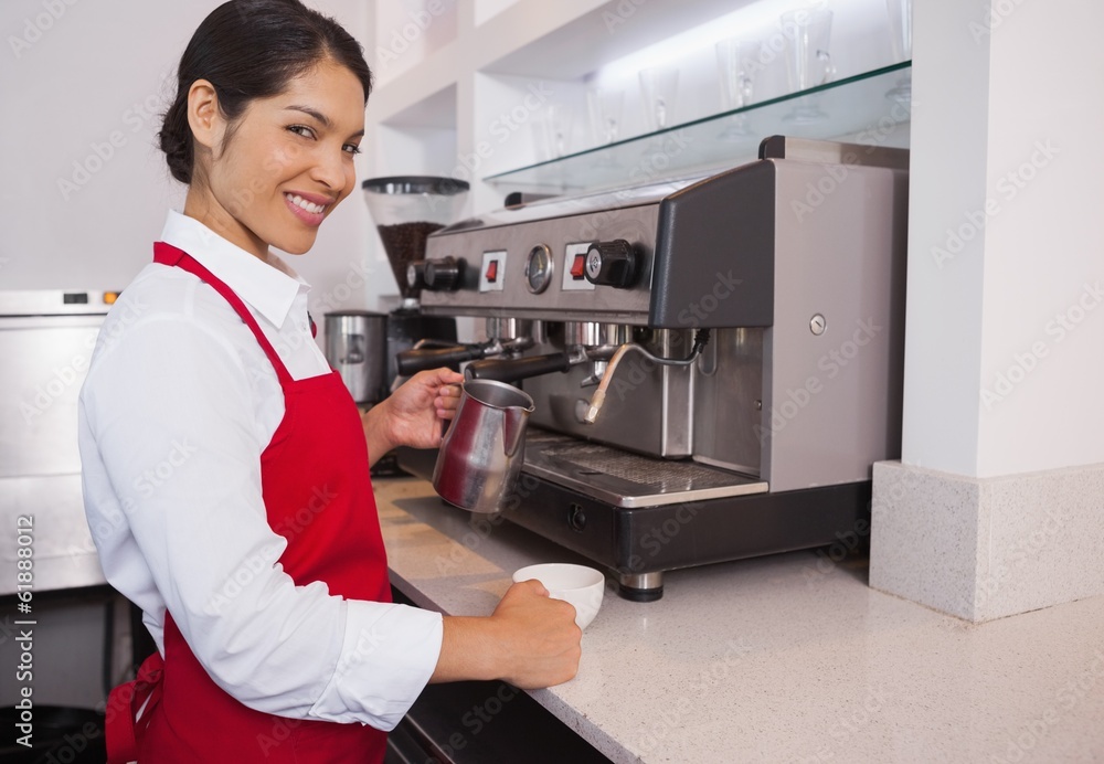 Pretty barista pouring milk into cup of coffee smiling at camera