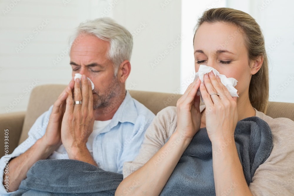 Sick couple blowing their noses sitting on the couch Sick couple blowing their noses sitting on the couch