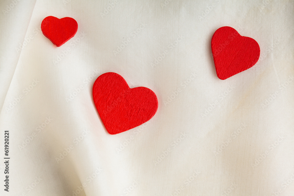 Red wooden decorative hearts on white silk background.