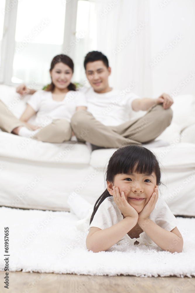 .Young Chinese girl in a living room with parents in the backgro .Young Chinese girl in a living room with parents in the backgro