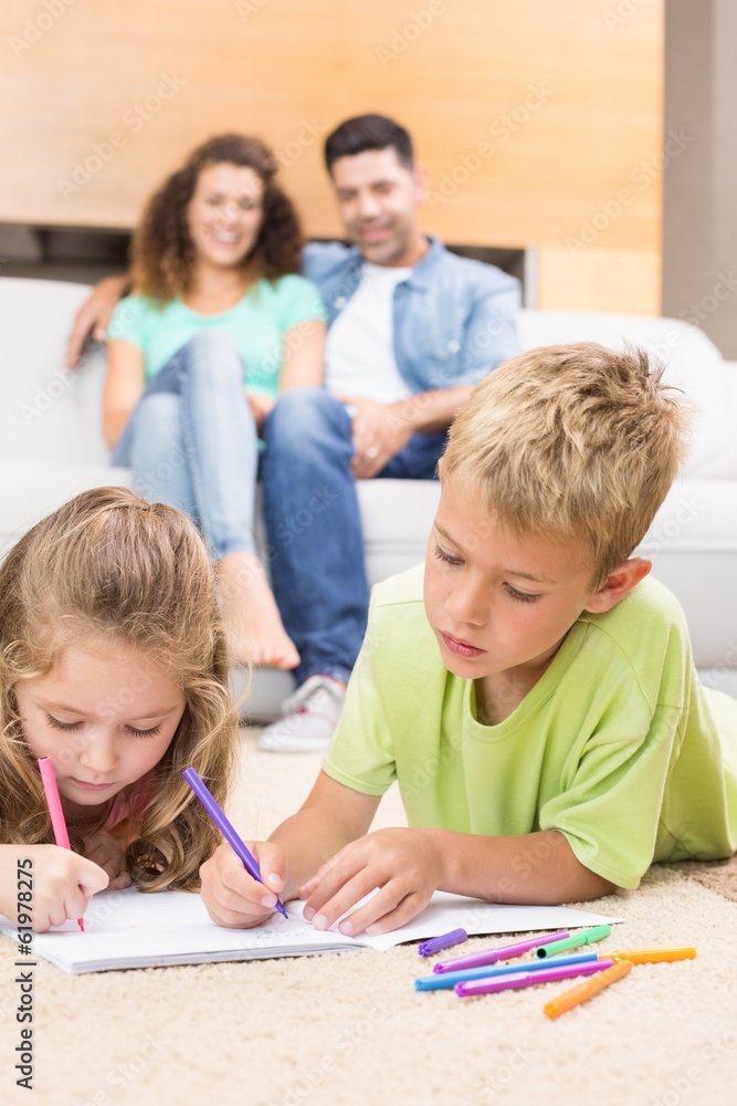 Siblings colouring on the rug with parents watching from sofa Siblings colouring on the rug with parents watching from sofa